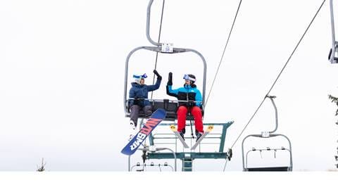 Two people sitting on a ski lift.
