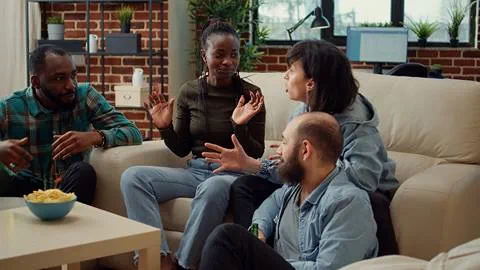 A group of people sitting on a couch talking to each other.