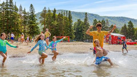 Children playing and splashing in water on a sunny beach with trees and a clear blue sky in the background.
