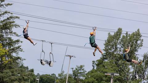 Three individuals zip-lining with a ski lift in the background.