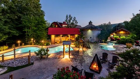 Evening view of an illuminated luxury backyard with a swimming pool, gazebo, and adjacent buildings.