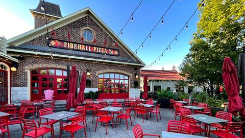 Exterior of fire hall pizza co. with red outdoor seating under string lights, set against a clear sky at dusk.