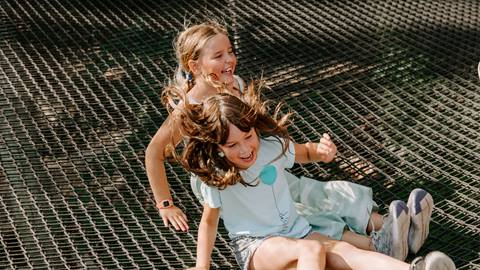 Two children laughing while sliding down a slope on a sunny day.