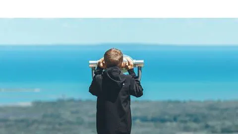 A child using binoculars to look at a distant scenery by the coast.