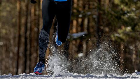 man running snowy trail in forest splashes- of snow