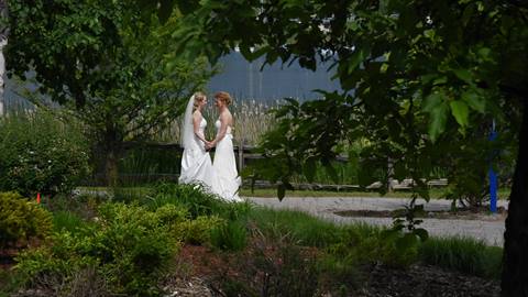 Two individuals in wedding attire embracing in a lush garden.