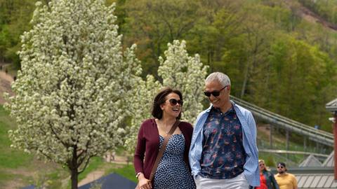 A smiling couple walking outdoors near a blooming tree on a sunny day.