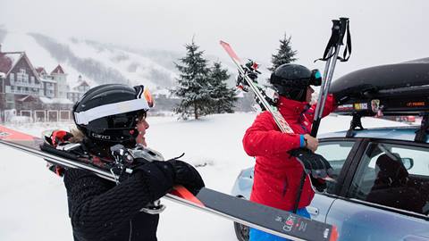 Two people holding their skis by the car