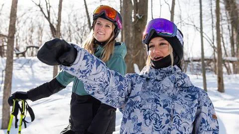 Two women wearing skis in the woods.