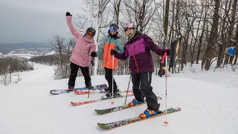 Three friends skiing and smiling at the top of Blue Mountain