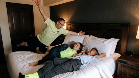 A family laying on a bed in a hotel room.