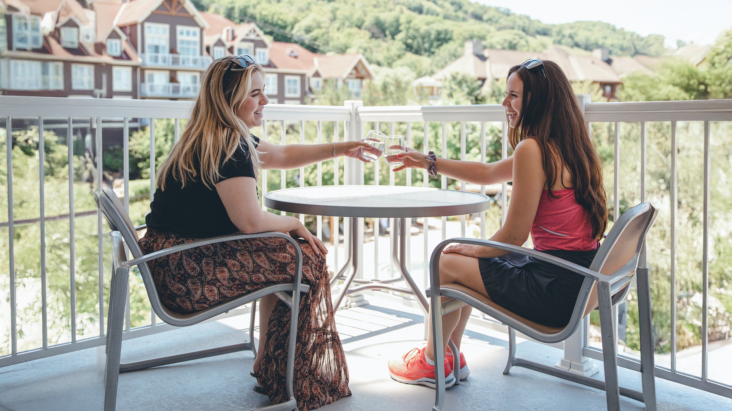 A man and woman talking on a balcony overlooking a ski resort.