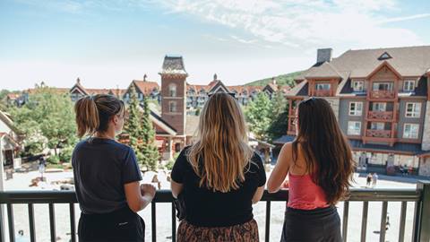 Three women smiling and enjoying each other's company on a sunny day outdoors.