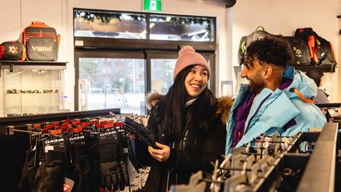 A man and woman looking at ski gear in a store.