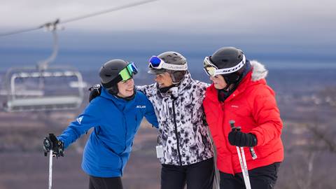 Three people in ski jackets standing in front of a ski lift.