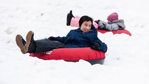 Two children riding on snow tubes in the snow.
