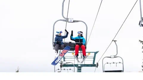 Two people sitting on a ski lift.