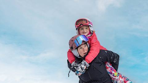 A woman carrying a child on her shoulders while skiing.