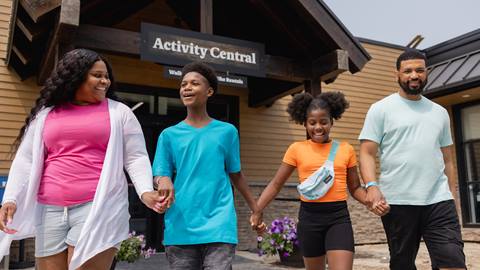 A family of four walking hand in hand near the "activity central" building, smiling and enjoying themselves.