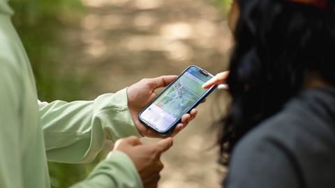Two individuals using a smartphone to navigate a map application while outdoors.