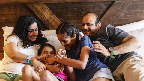 A family sits on a bed and smiles at each other.