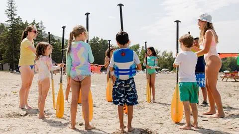 A group of kids holding a paddle in a circle at the Blue Mountain Private Beach
