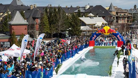A man jumping into a pool with a crowd watching.