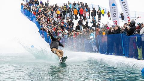 A man riding a snowboard down a water slide in front of a crowd.