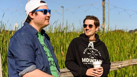 Two men standing side by side, with tall grass in the background.