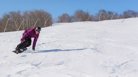 A man in a purple jacket snowboarding down Blue Mountain Resort