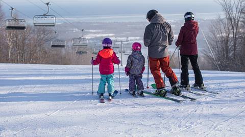 A family in full ski attire, standing at the top of the hill