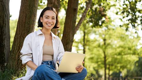 A woman sitting in the grass with her legs crossed and a laptop.