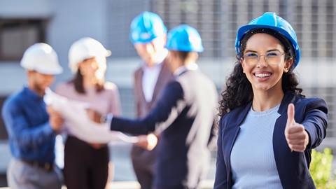 A woman in a hard hat is giving a thumbs up.