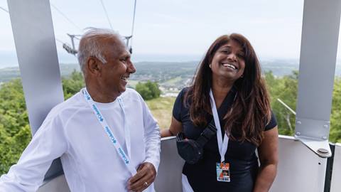 Two people smiling inside a cable car with a scenic landscape in the background.