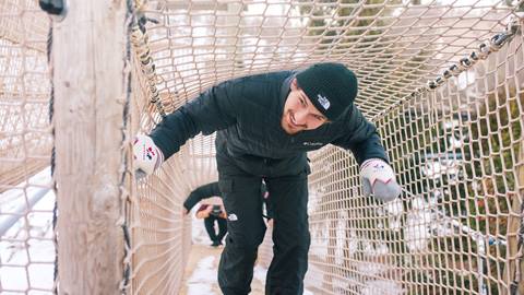 A man is climbing up a rope in a snowy area.