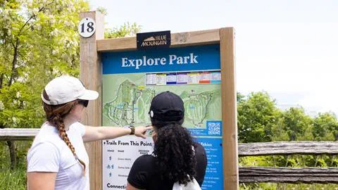 Two women pointing to a map at a park.