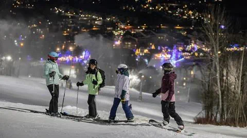 Group of skiers and snowboarders on run at Blue Mountain overlooking the village during night skiing.