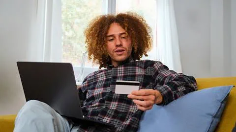 A man sitting on a couch with a laptop and credit card.