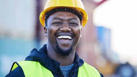 A smiling man wearing a hard hat and vest.