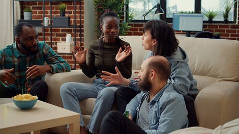 A group of people sitting on a couch talking to each other.