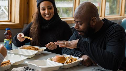 A man and a woman smiling and enjoying a meal of fried chicken and fries at a table in a well-lit dining area.