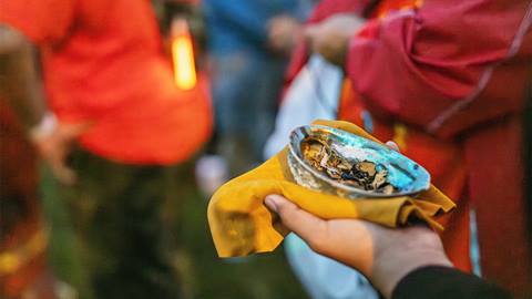 Person holding a small bowl with burnt incense and herbs during a group outdoor ceremony.