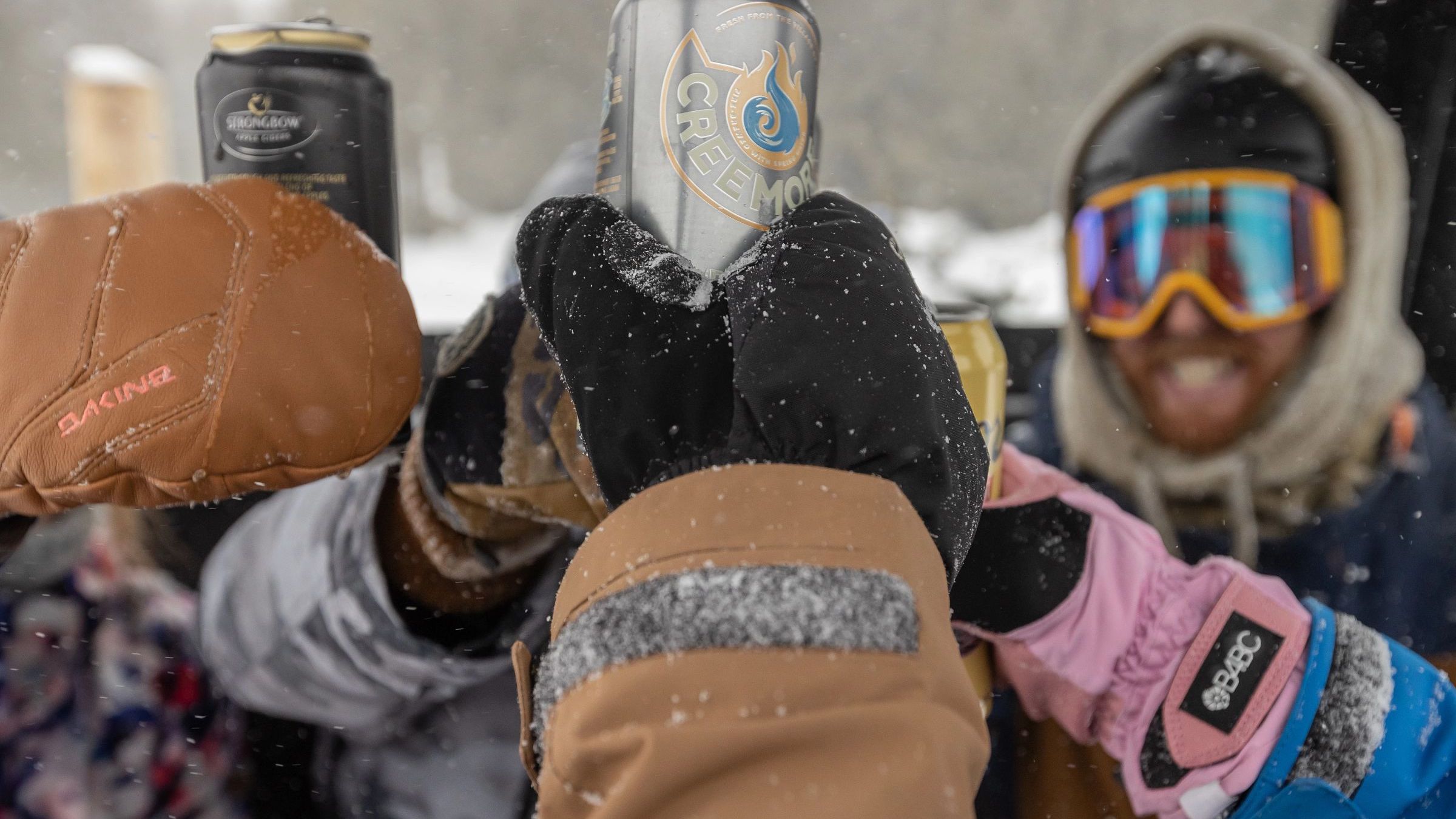 Man smiling with goggles while cheersing others with gloves and ski jackets