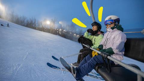 Pair of friends sitting on chairlift during night skiing at Blue Mountain