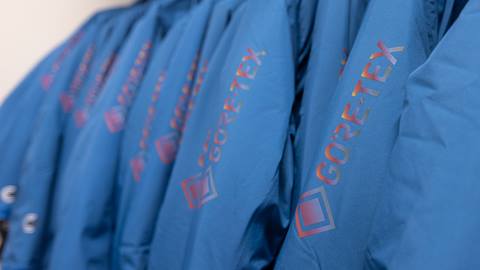 Close-up of several blue jackets with "GORE-TEX" logos in red letters, hanging in a row.