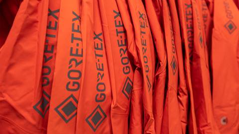 Close-up of several orange jackets hanging in a row, each labeled with "GORE-TEX" in black text.