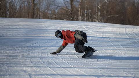 Person in red jacket and black helmet snowboarding down a snowy slope, touching the ground with one hand.