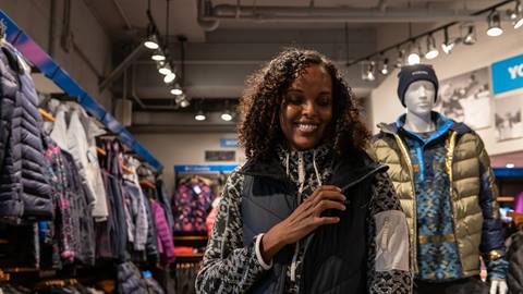 A woman smiles while standing in a clothing store.