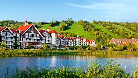 Idyllic resort with tudor-style architecture nestled by a lake with a lush green hill in the background.