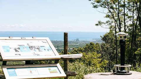 A scenic overlook with an informational sign and a coin-operated telescope facing a vast body of water.